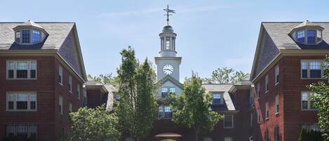 A large brick building with a central tower featuring a clock and a weather vane.