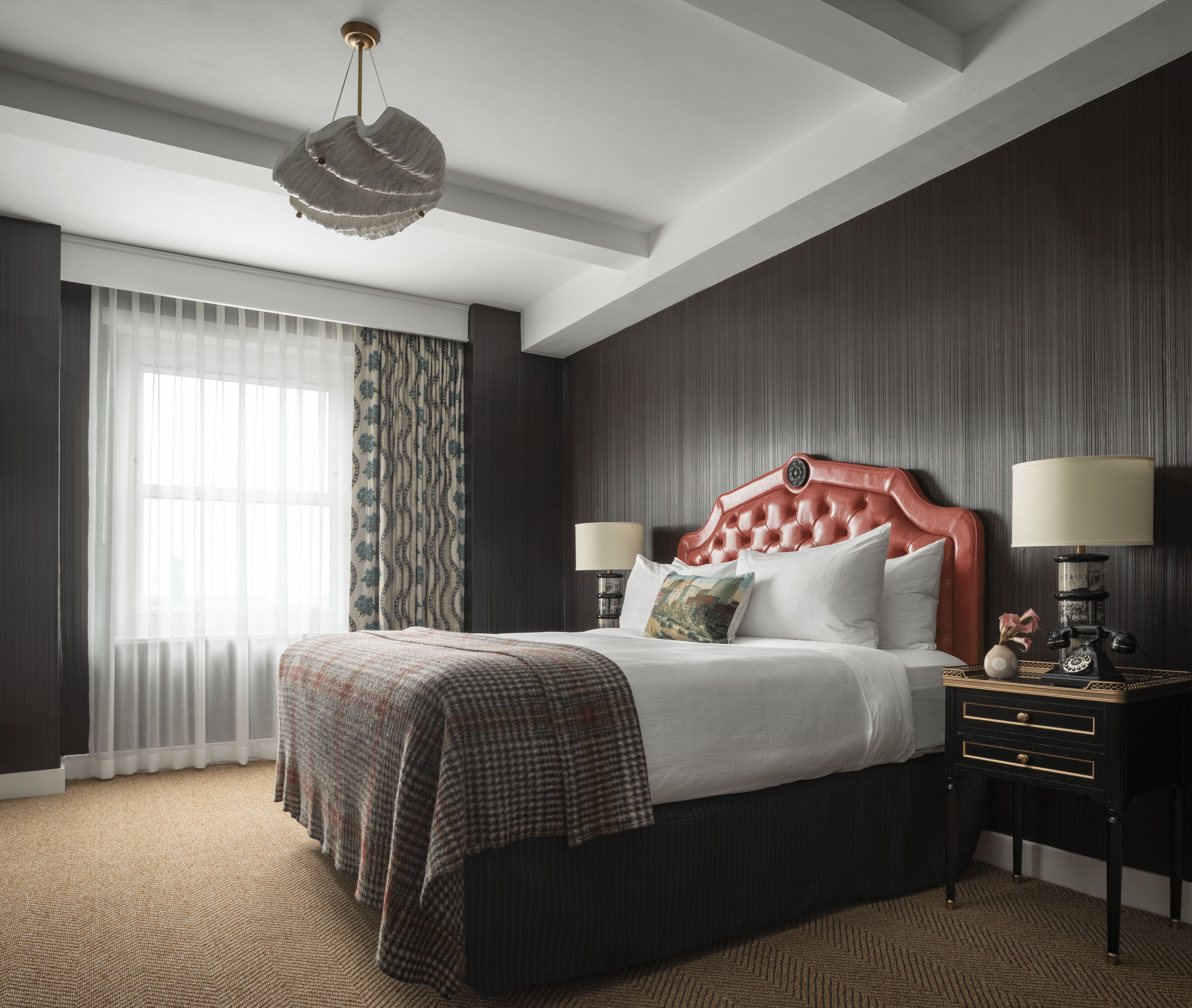 A hotel room with a large bed, two bedside tables, a chandelier, and a view of the outdoors through the window.
