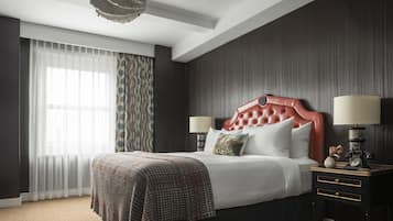 A hotel room with a large bed, two bedside tables, a chandelier, and a view of the outdoors through the window.