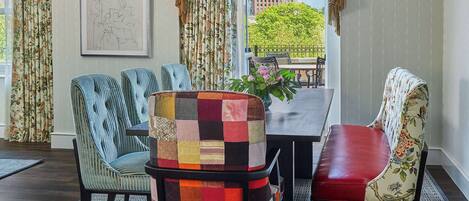 A dining area with a table and chairs, a hanging light fixture, and a view of buildings and trees outside.