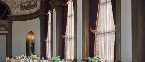 A banquet hall with round tables, gold chairs, and a patterned carpet.