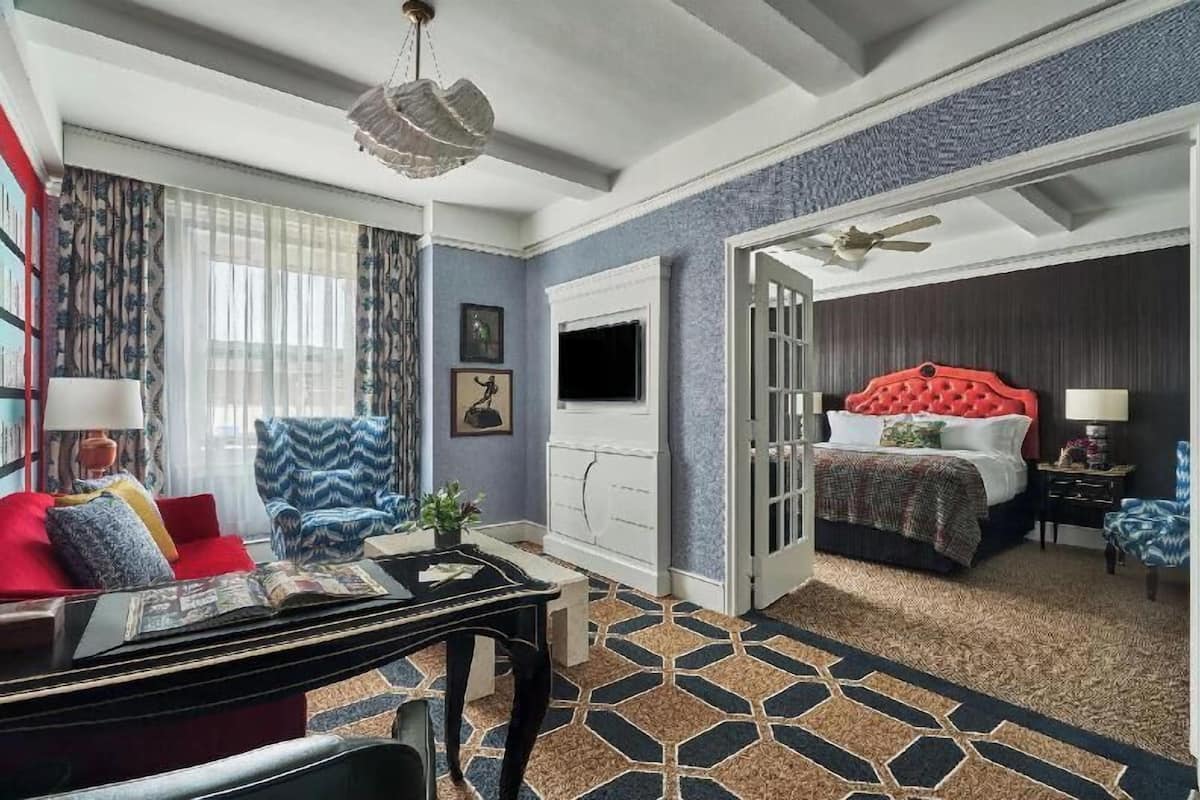 Une chambre d’hôtel équipée d’un lit, d’un bureau, d’une chaise, d’une télévision et d’une porte donnant sur une autre pièce.