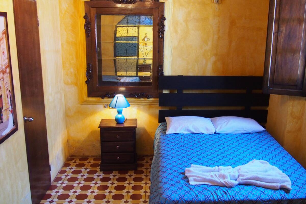 A bedroom with a bed, a nightstand with a lamp, a window, and a door.