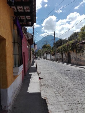 Une rue pavée bordée d’immeubles, un ciel dégagé et des montagnes à l’horizon.