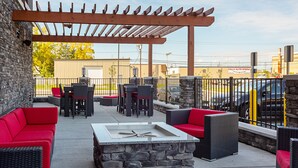 Un patio al aire libre con paredes de piedra, muebles de mimbre rojo y negro, y una chimenea central.