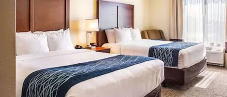 A hotel room with two beds, a desk, a chair, and a window with curtains.