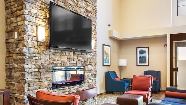 Pared de piedra con un televisor de pantalla plana, una chimenea y asientos con cojines rojos y azules.