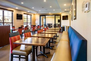 A dining area with multiple tables and booths, large windows, and a television mounted on the wall.