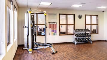 Centro de fitness com área de musculação, suporte para halteres e um painel com cartazes informativos.