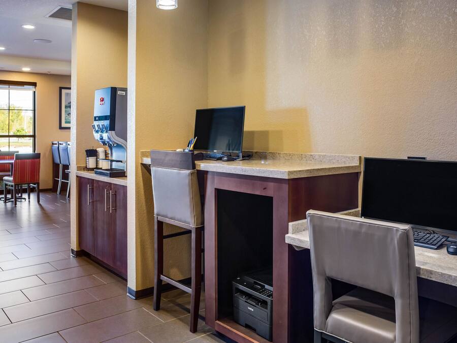 A hotel room with a desk, computer, and coffee machine. There are chairs and a window with a view of trees.