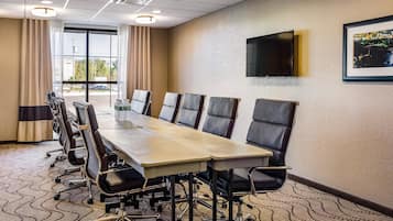 A conference room with a long table, chairs, a TV on the wall, and a window with curtains.