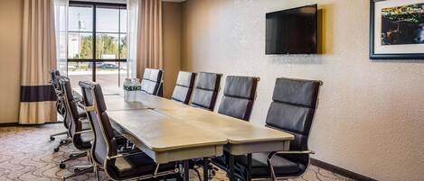 A conference room with a long table, chairs, a TV on the wall, and a window with curtains.