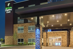 Un hotel Holiday Inn Express & Suites con fachada moderna, revestimiento de piedra y señalización iluminada.