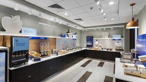 A modern breakfast area with a self-serve station, a large apple-shaped sign, and a kitchen display. - Holiday Inn Express & Suites West Des Moines - Jordan Creek by IHG (West Des Moines)