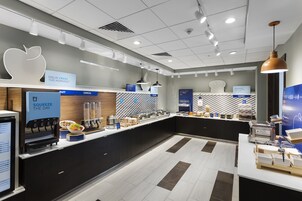 Un área de desayuno moderna con una estación de autoservicio, un letrero grande con forma de manzana y una vitrina de cocina.