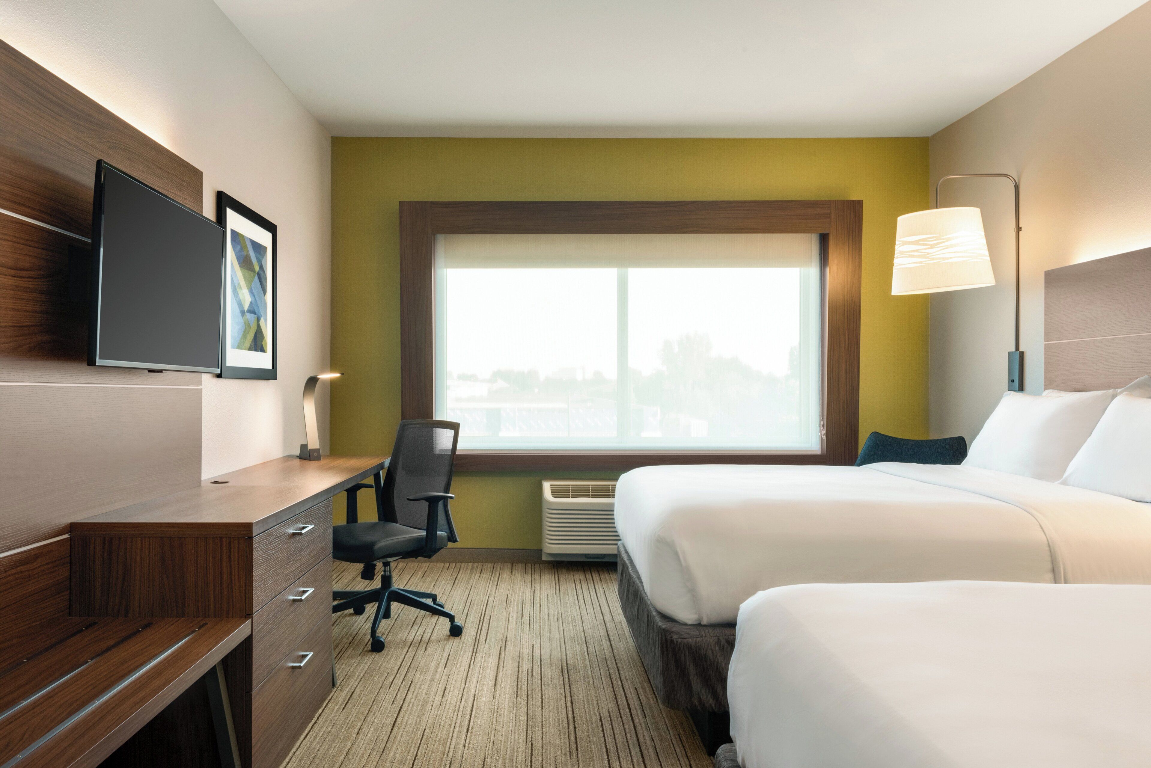 A hotel room with a bed, a desk with a chair, a TV, and a window with a city view.