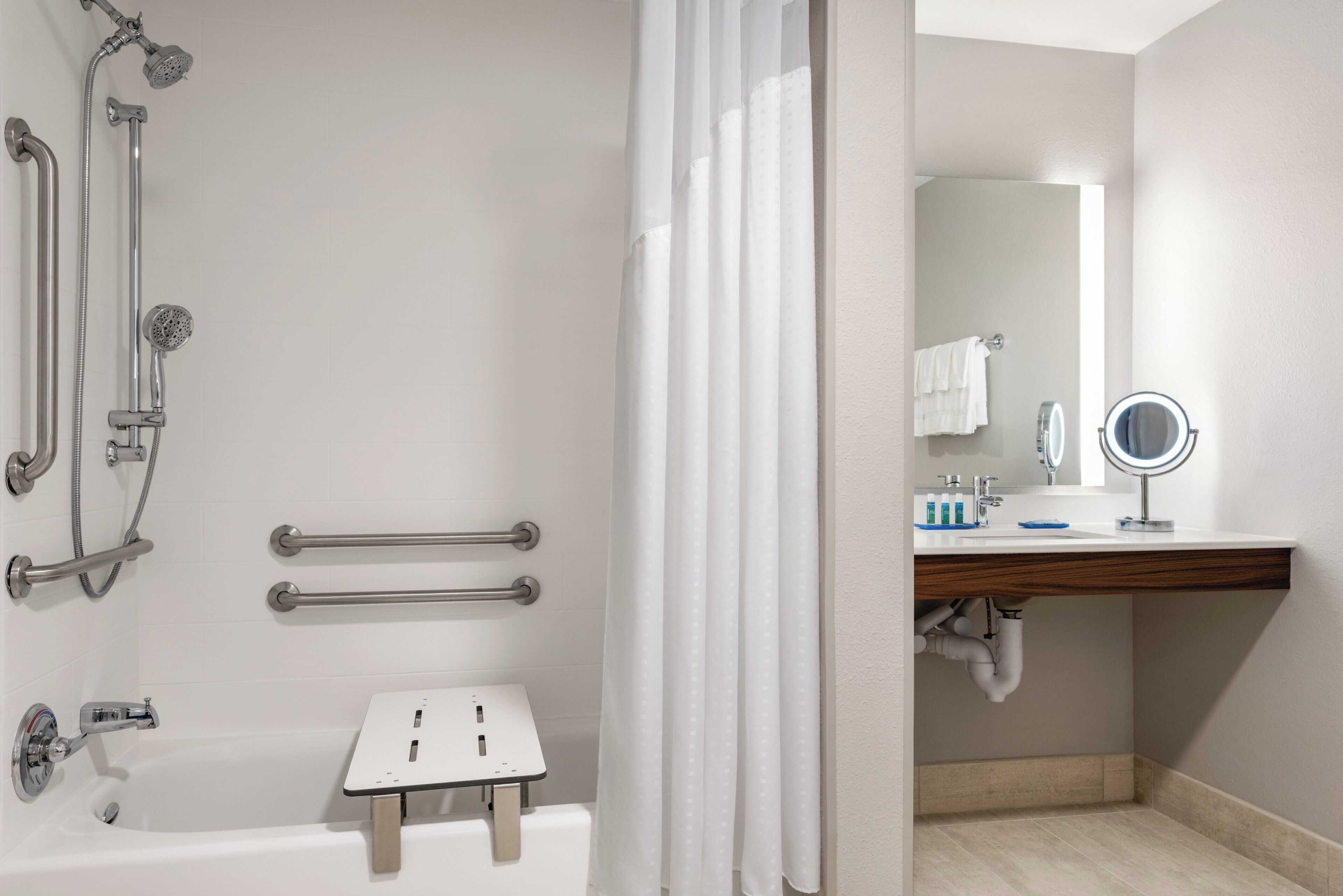 A modern bathroom with a bathtub, shower, and handrails.