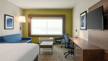 Habitación de hotel con cama, escritorio, silla, sofá, ventana y televisión de pantalla plana.
