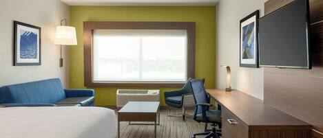 Habitación de hotel con cama, escritorio, silla, sofá, ventana y televisión de pantalla plana.