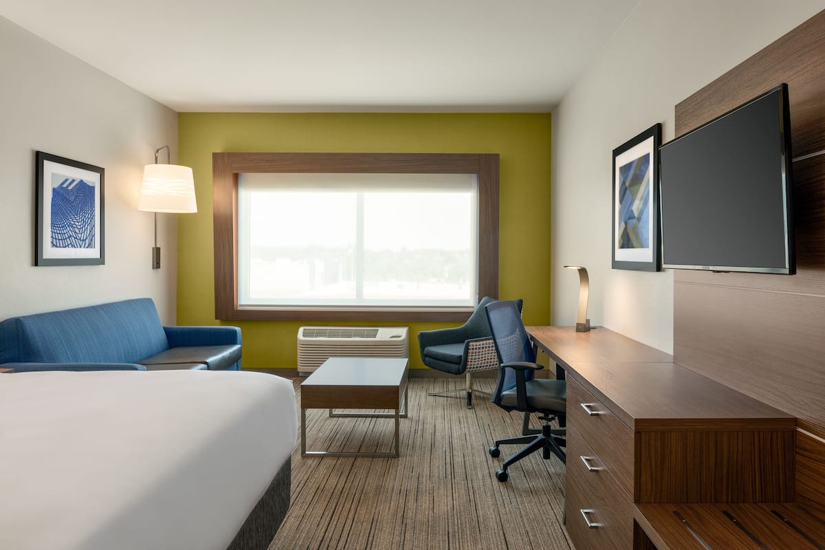 Habitación de hotel con cama, escritorio, silla, sofá, ventana y televisor de pantalla plana.