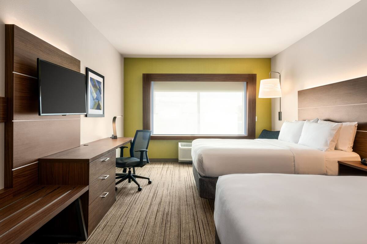 Ein Hotelzimmer mit Schreibtisch, zwei Betten, Fernseher, Fenster und Lampe.