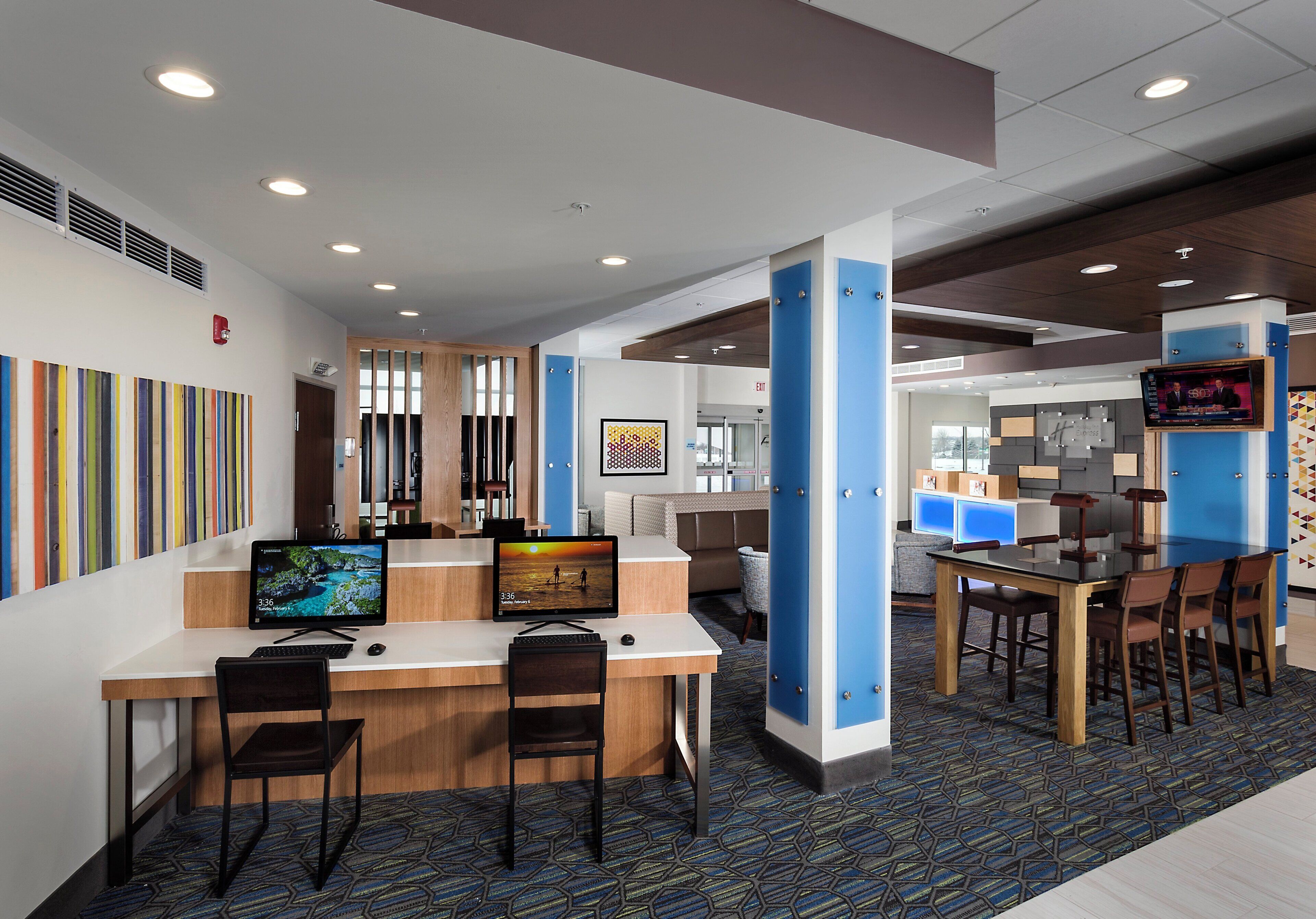 A modern hotel lobby with a reception desk, seating area, and a television screen displaying a news program.