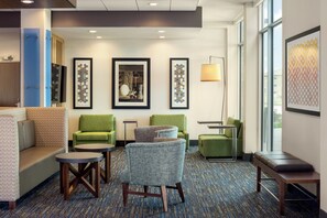 A hotel lobby with green armchairs, a sofa, a small table, and framed artwork on the walls. - Holiday Inn Express & Suites West Des Moines - Jordan Creek by IHG (West Des Moines)