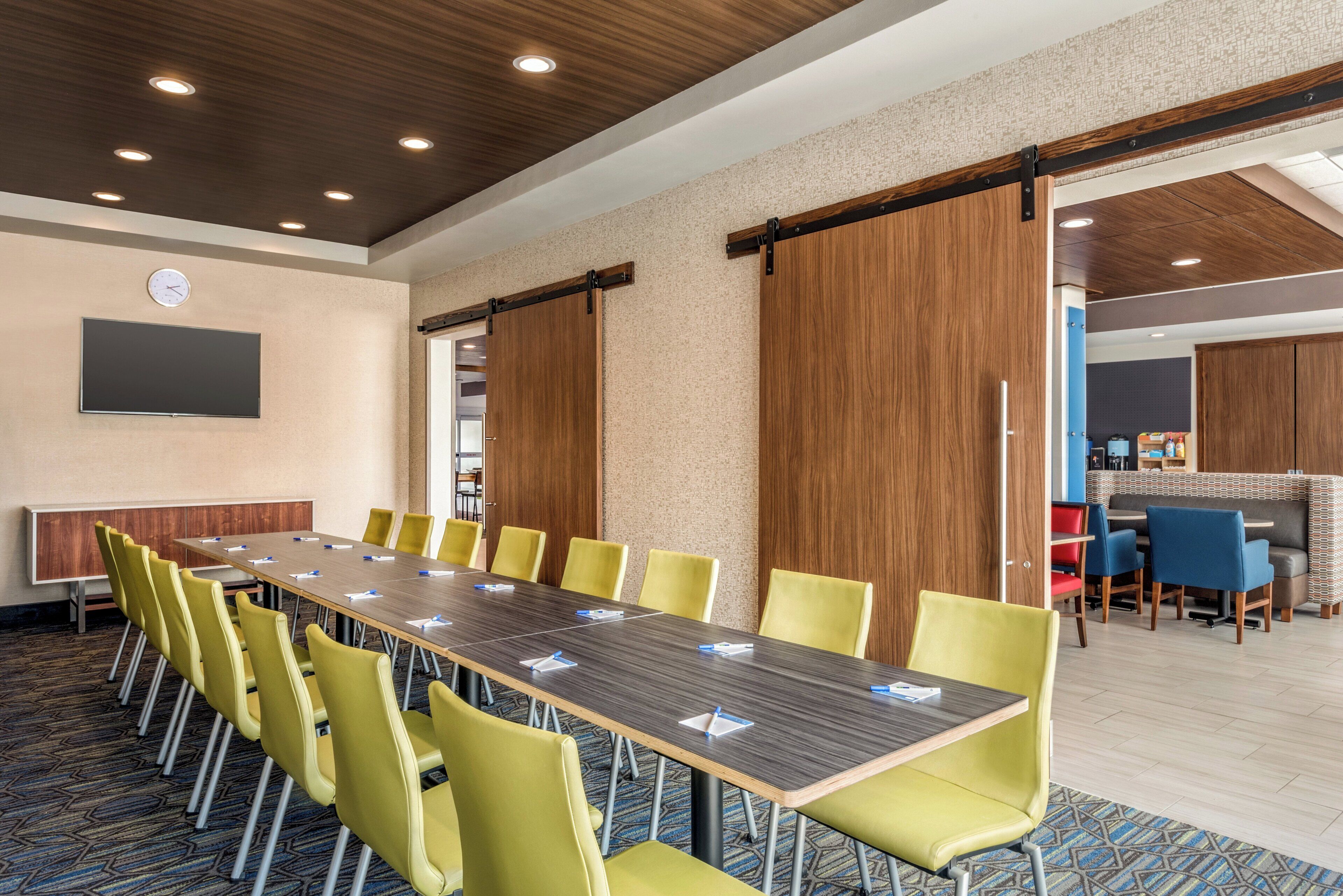 A conference room with a long table, yellow chairs, and a clock on the wall.