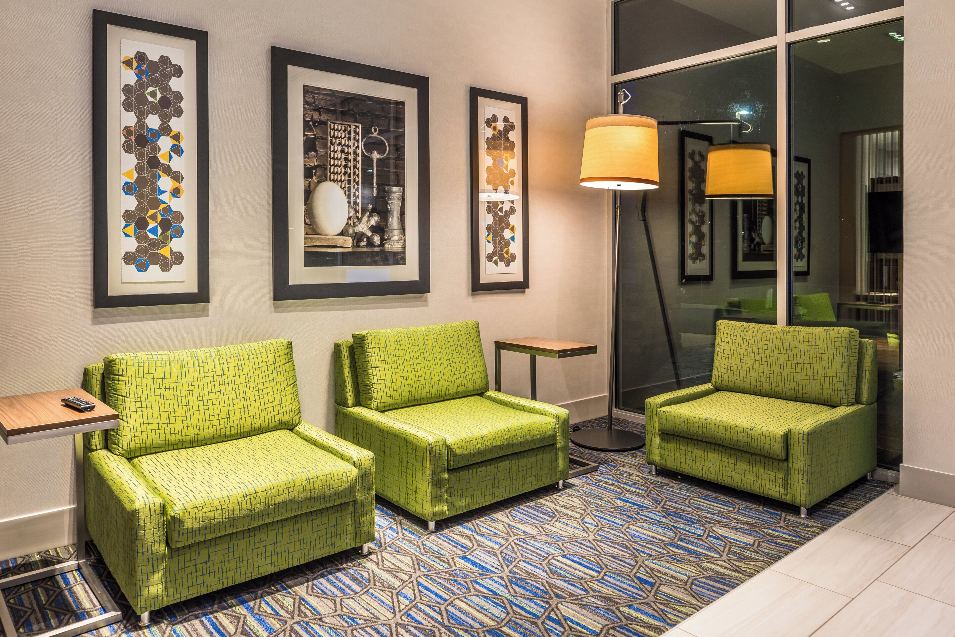 Vestíbulo de hotel con tres sillones verdes, una lámpara de pie y cuadros en la pared.
