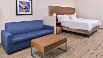 Een hotelkamer met een blauwe bank, een houten bijzettafeltje, een bed met wit beddengoed en een lijst met een abstract schilderij aan de muur.