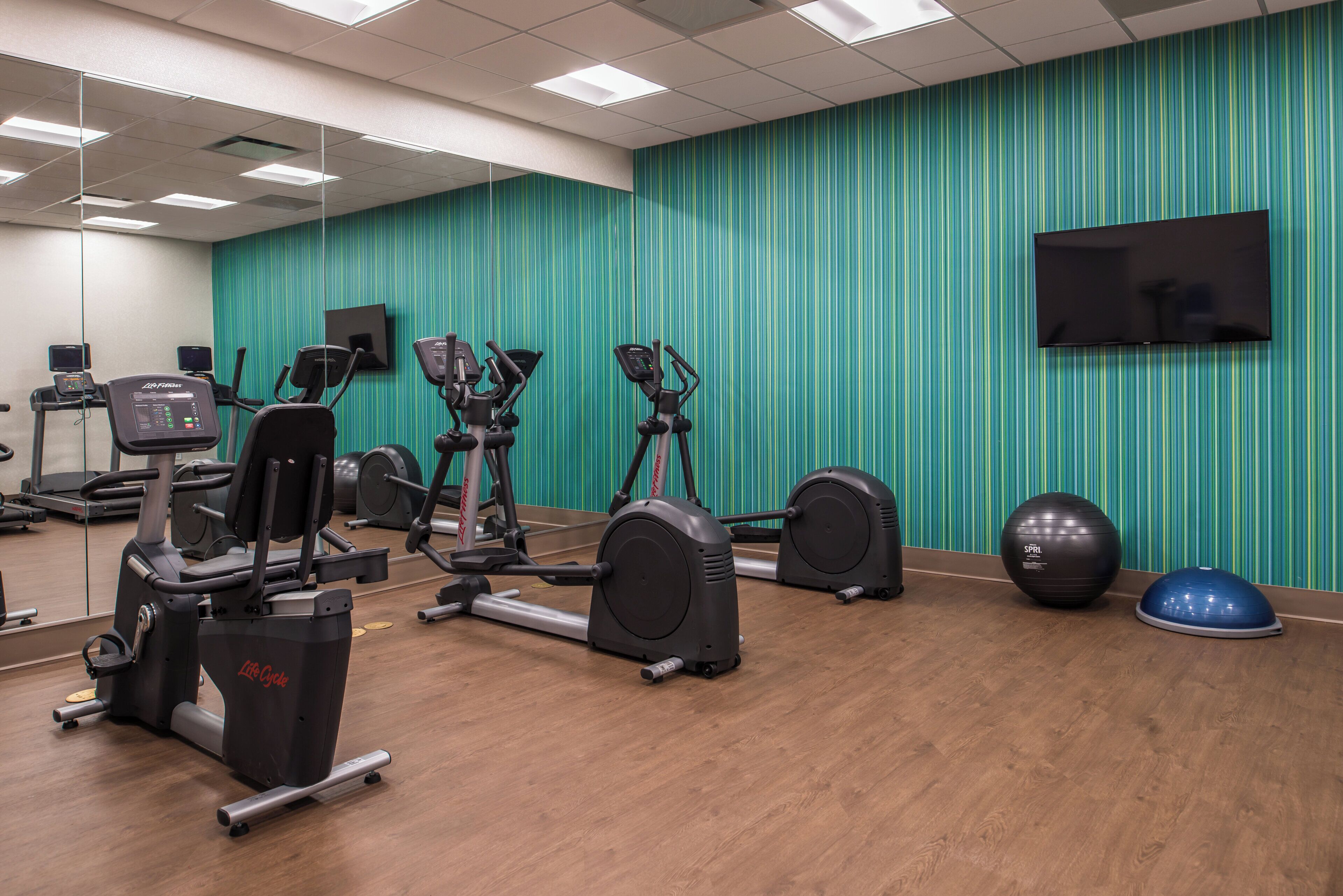 Un gimnasio con equipo de ejercicio, televisión y espejo.
