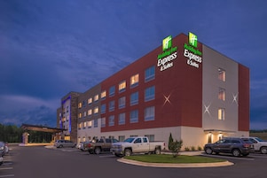 Um hotel Holiday Inn Express & Suites com design moderno, várias vagas de estacionamento e céu claro.