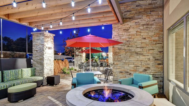 An outdoor patio area with a stone wall, a fire pit, and outdoor seating. - Home2 Suites by Hilton Springfield North (Springfield)