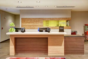 A hotel reception desk with a wooden counter, a digital check-in station, and a sign indicating the hotel name. - Home2 Suites by Hilton Springfield North (Springfield)