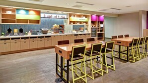 A modern restaurant with a long counter, multiple seating areas, and a variety of tableware displayed on shelves. - Home2 Suites by Hilton Springfield North (Springfield)