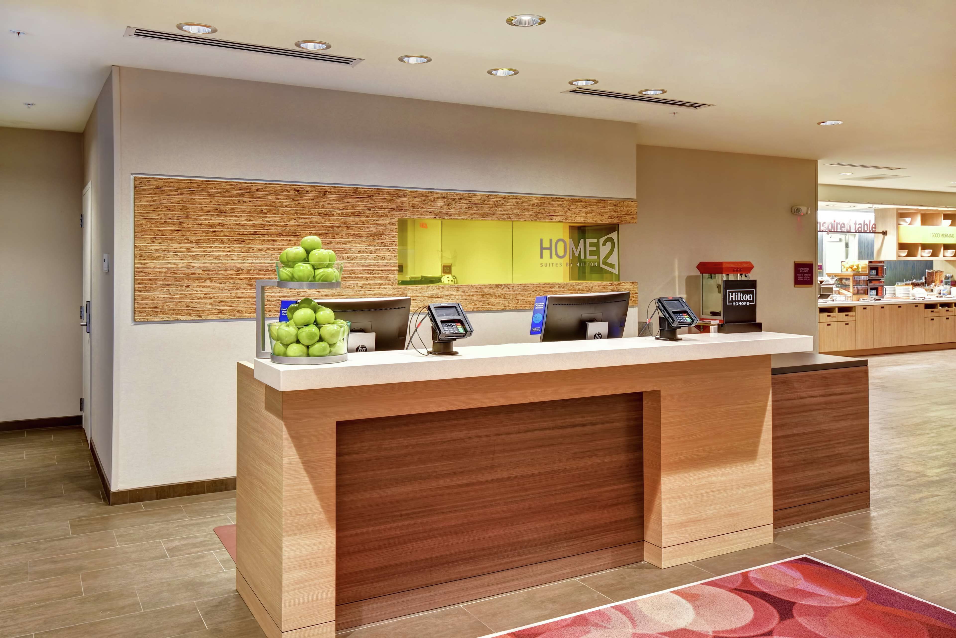A hotel reception desk with a modern design, a digital check-in station, and a view of the hotel's interior.