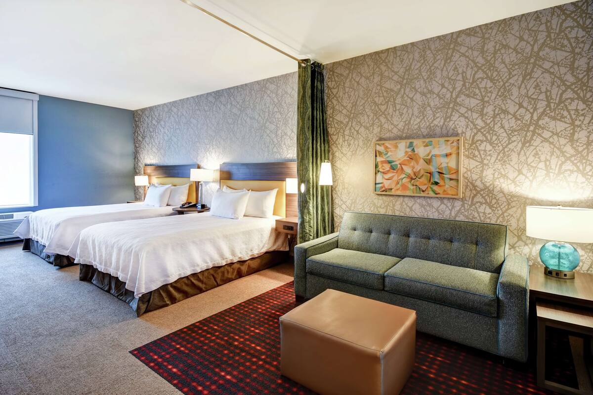 A hotel room with two beds, a green sofa, a red patterned rug, and a painting on the wall.