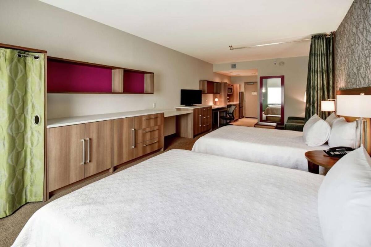 A hotel room with two beds, a kitchenette, a TV, and a mirror.