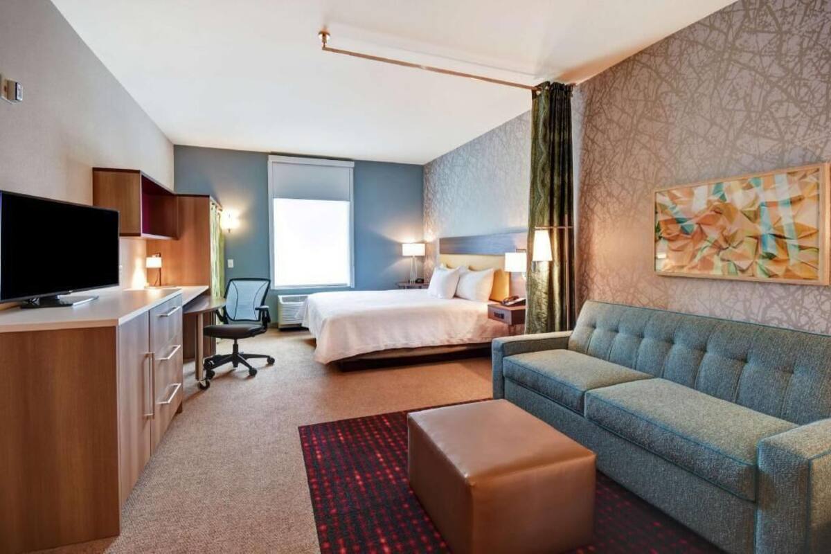 A hotel room with a bed, a sofa, a desk with a TV, and a chair.