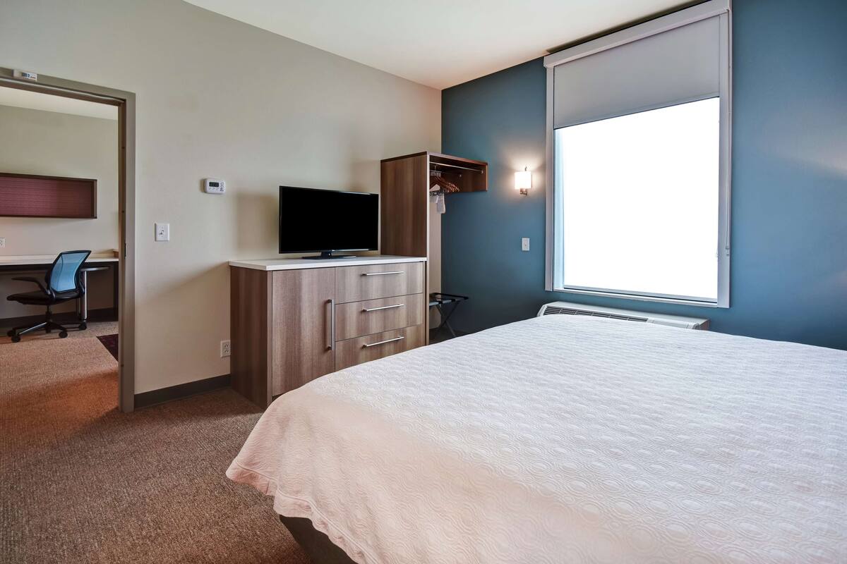 A hotel room with a bed, a desk with a chair, a television, a wardrobe, and a window with a view.