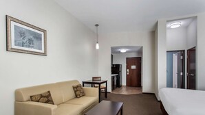 A hotel room with a sofa, a small table, a bed, a framed picture on the wall, and a kitchenette in the background. - MainStay Suites Big Spring North I-20 (Big Spring)