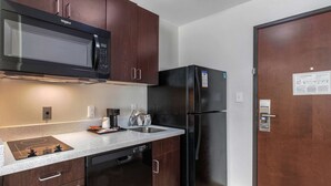 A compact kitchen with dark wood cabinets, a black microwave, a refrigerator, and a dishwasher. - MainStay Suites Big Spring North I-20 (Big Spring)