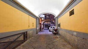 Un couloir étroit aux murs jaunes et au sol carrelé, qui mène à un escalier et à un véhicule garé au bout.