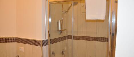 Une douche fermée par des parois en verre, dotée d’un pommeau de douche à main et d’un porte-serviettes.