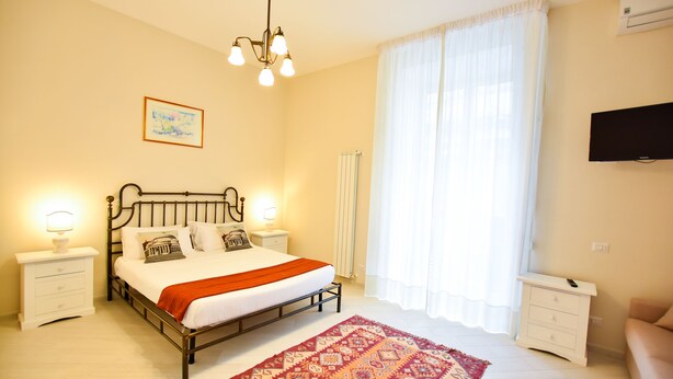 Une chambre à coucher avec un lit, des tables de chevet, une télévision et une fenêtre avec des rideaux.