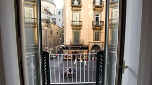 Une vue depuis un balcon donnant sur une rue bordée d’immeubles, avec un magasin appelé « Hugo Fama » et une clôture en métal.