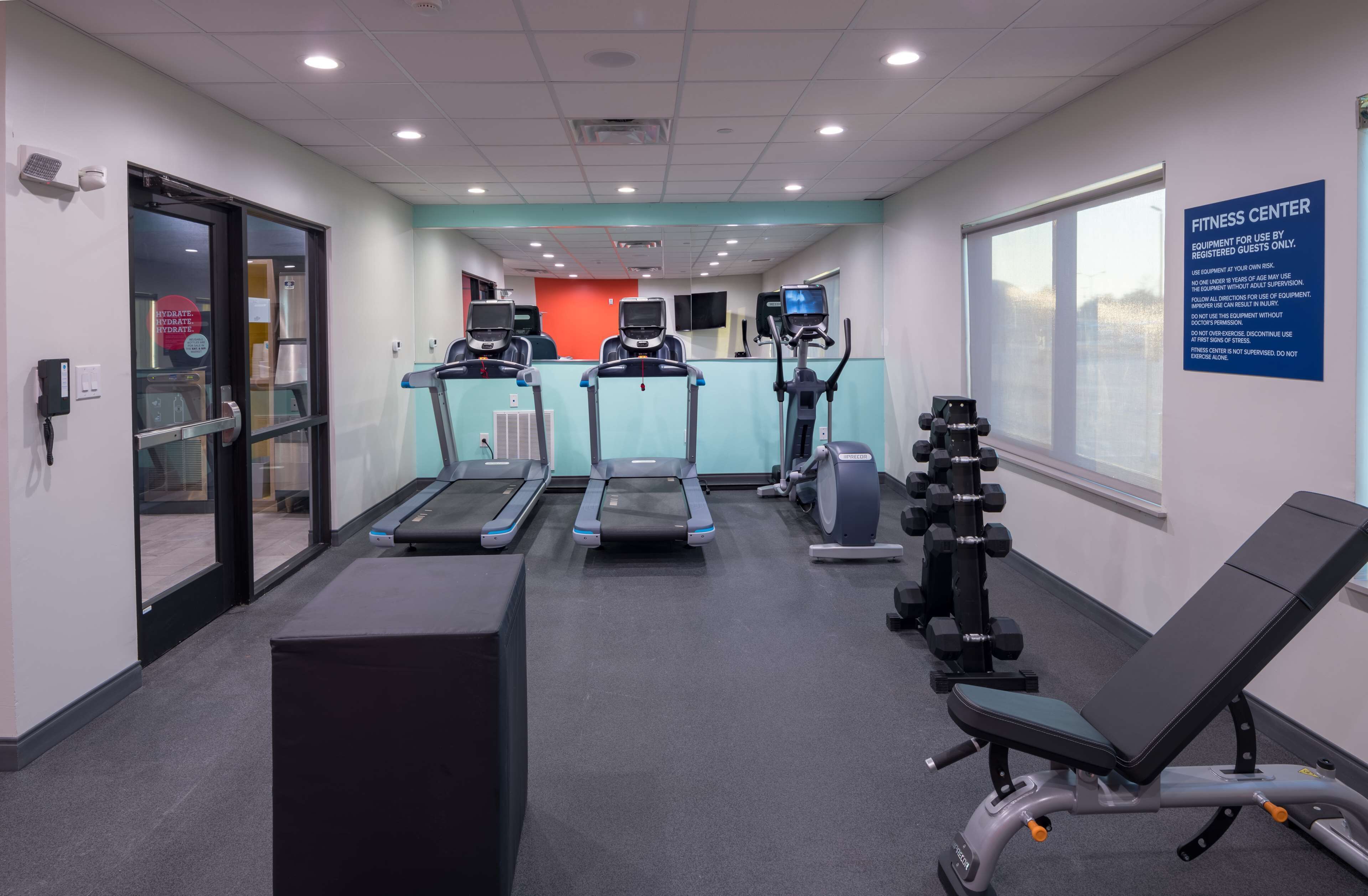 Un gimnasio equipado con cintas de correr, una banca y pesas.