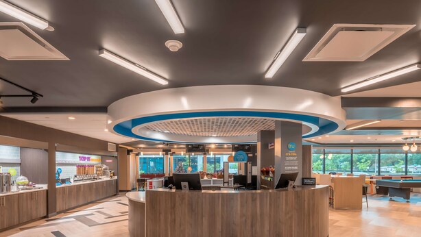 A modern hotel lobby with a central reception desk, a pool table, and a view of the outdoors. - Tru by Hilton Garland Richardson (Garland)