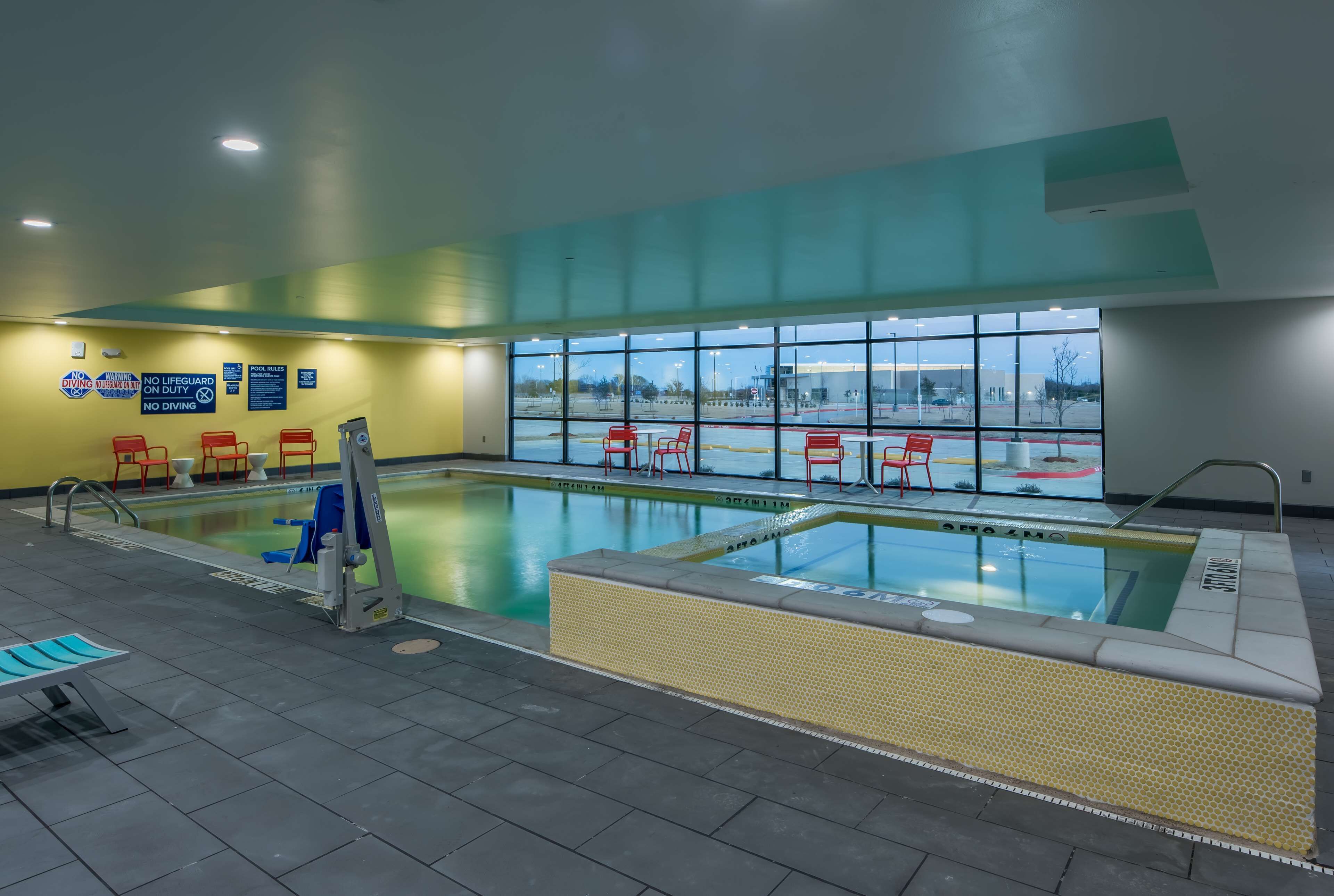 Piscina interna con segnaletica chiara, una postazione per il bagnino e vista sull'esterno attraverso ampie vetrate.