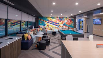 Un área de estar moderna con mesa de billar, asientos cómodos y un mural llamativo.